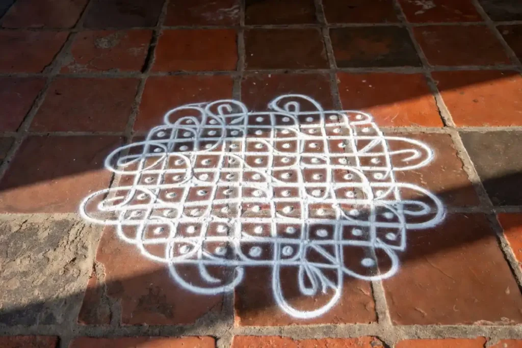 Cute small rangoli dot grid kolam design in white rice flour on terracotta floor