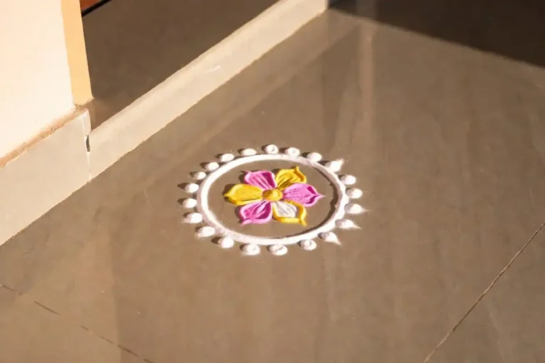 Cute small rangoli with pink and yellow floral design on a doorstep