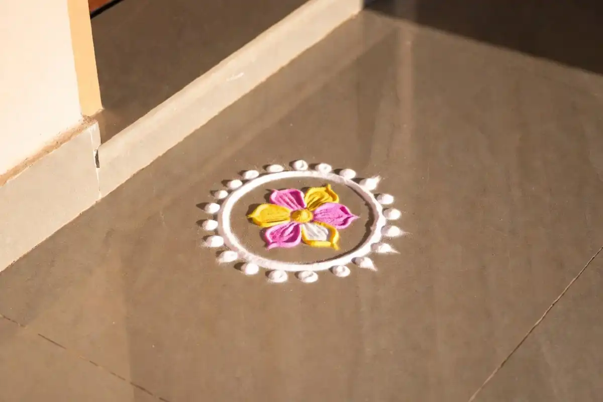Cute small rangoli with pink and yellow floral design on a doorstep