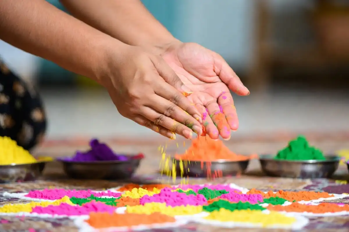 Hands creating a colorful Dhanteras rangoli design with rangoli powder