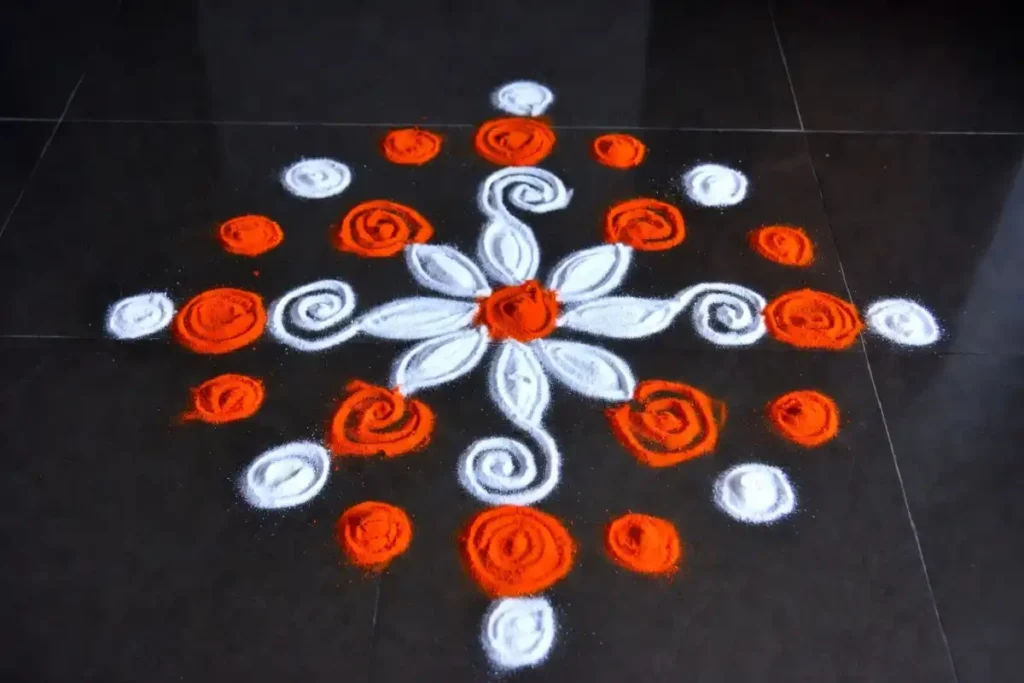 Beginner dot-based rangoli kolam pattern in white and orange on a dark floor viewed from above