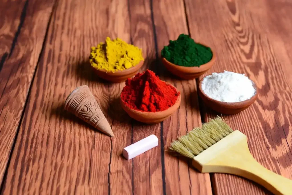 Tools and materials for making a dot rangoli design including colored powder, a rangoli cone, chalk, and a brush on a wooden surface