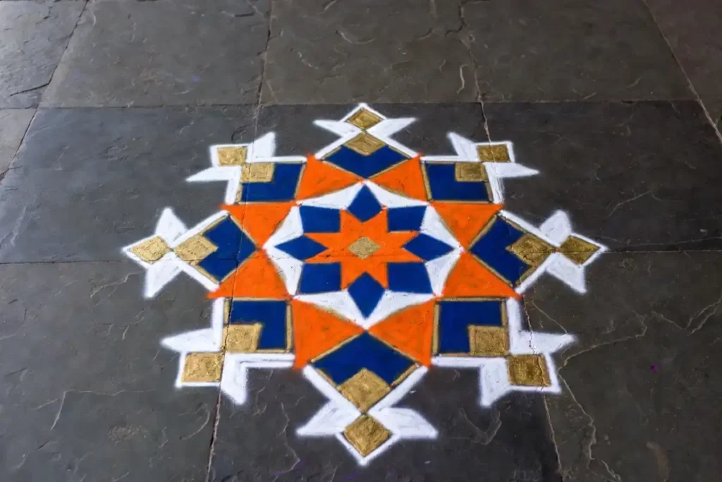 Geometric rangoli with star and diamond shapes in orange, white, blue, and gold colors