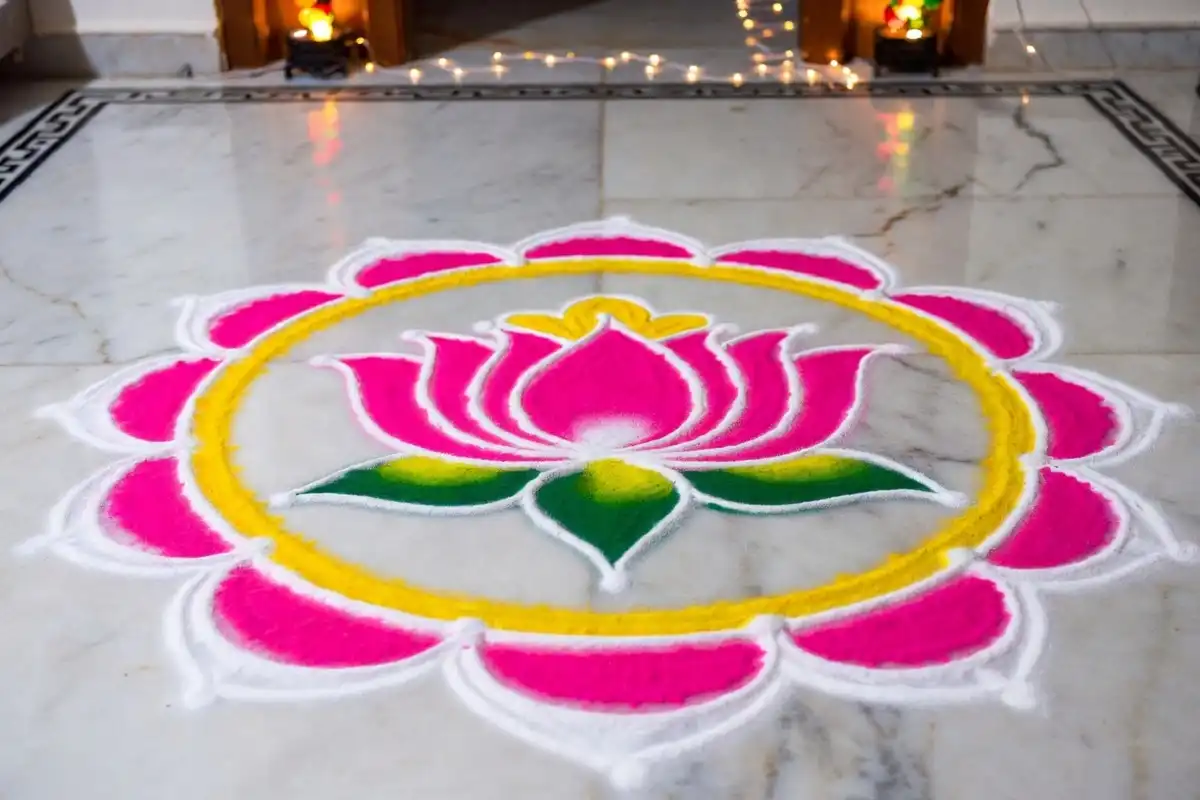 Vibrant pink and white lotus rangoli design with layered petals and yellow accents on marble floor