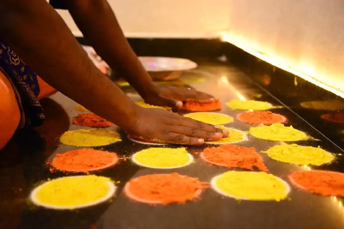 Hands filling a rangoli design easy dot-grid pattern with colored powder showing creation process