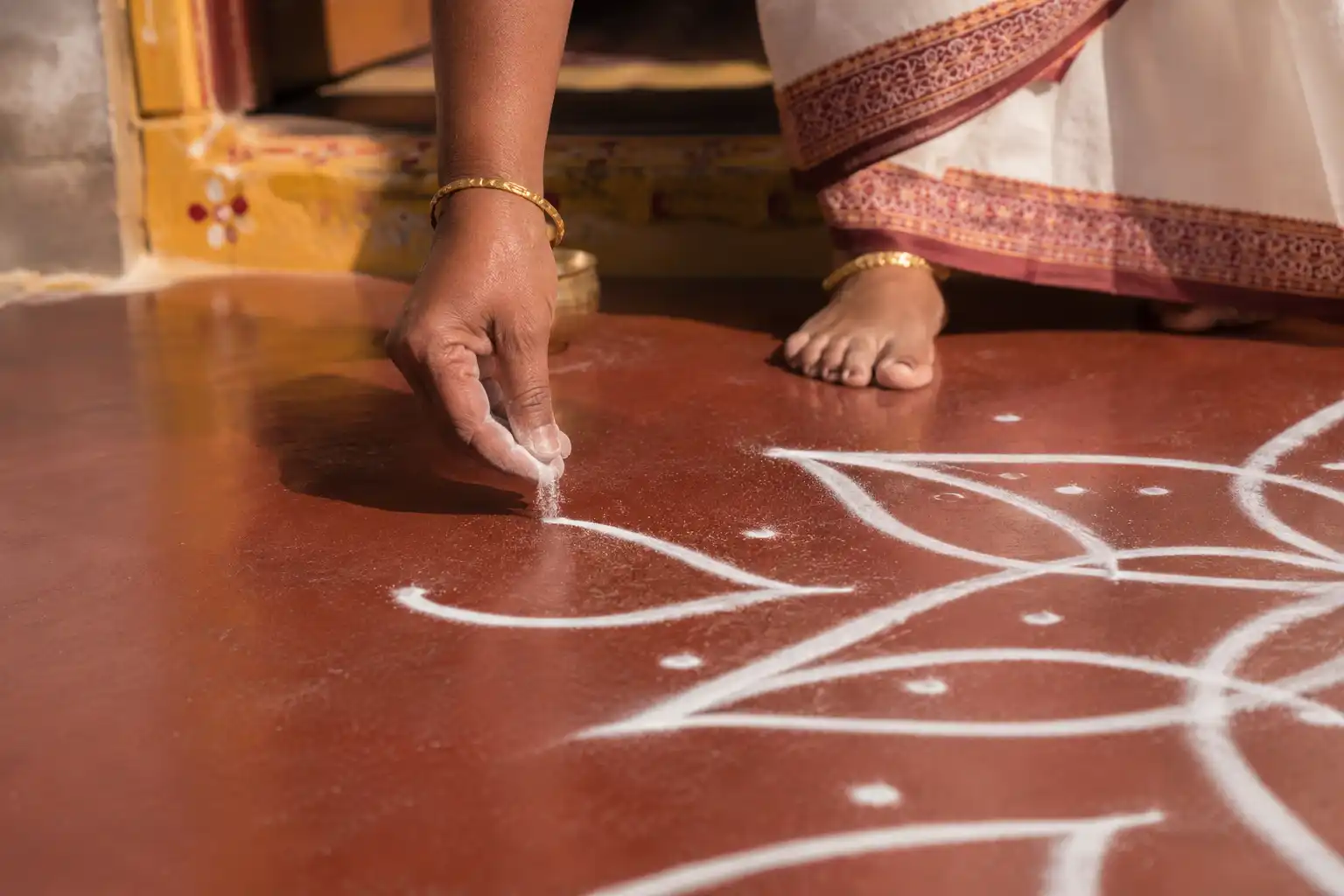 Traditional rangoli being drawn by hand with rice flour at the entrance of an Indian home
