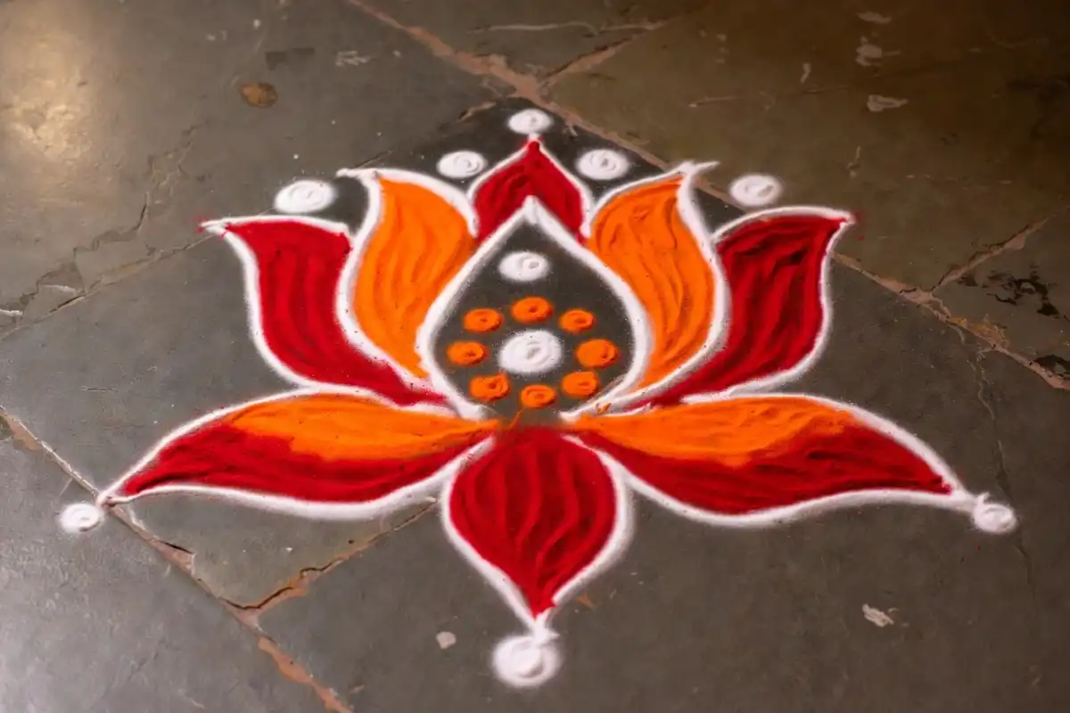 Simple beginner lotus rangoli design with red orange and white powder on dark stone floor