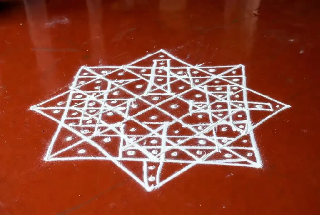 Small rangoli designs with dots in a kolam-style geometric star pattern on a red floor