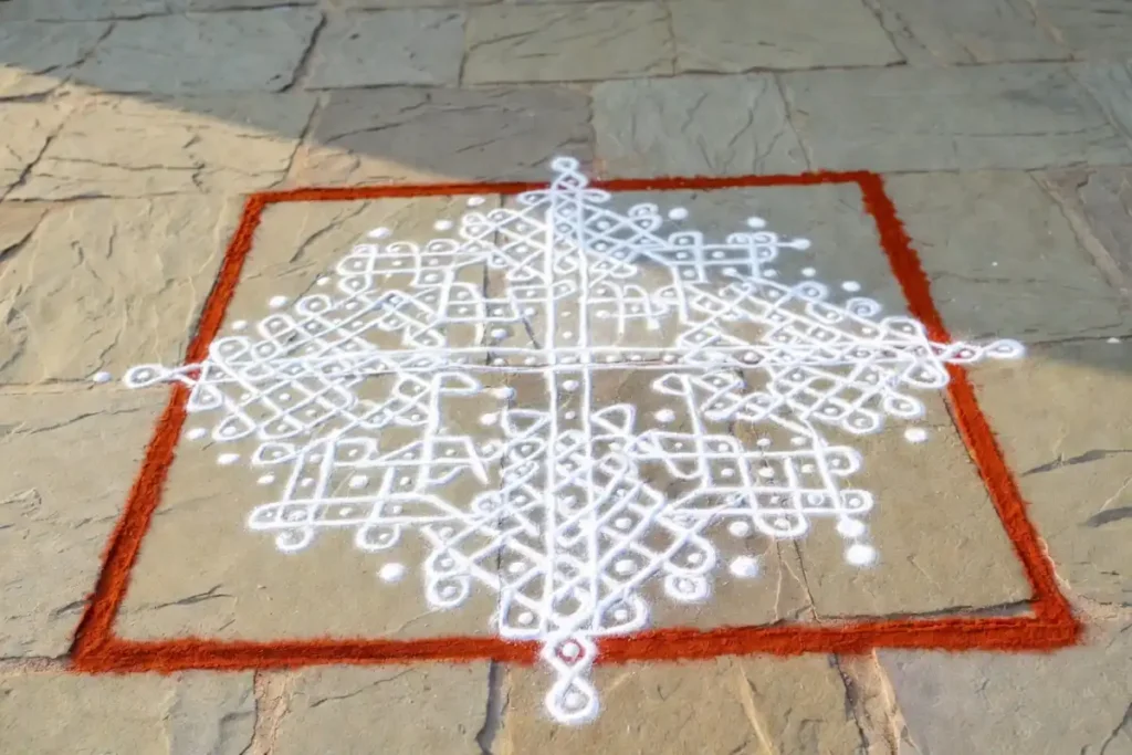 Traditional rangoli design with kolam dot pattern in white and red on a courtyard floor