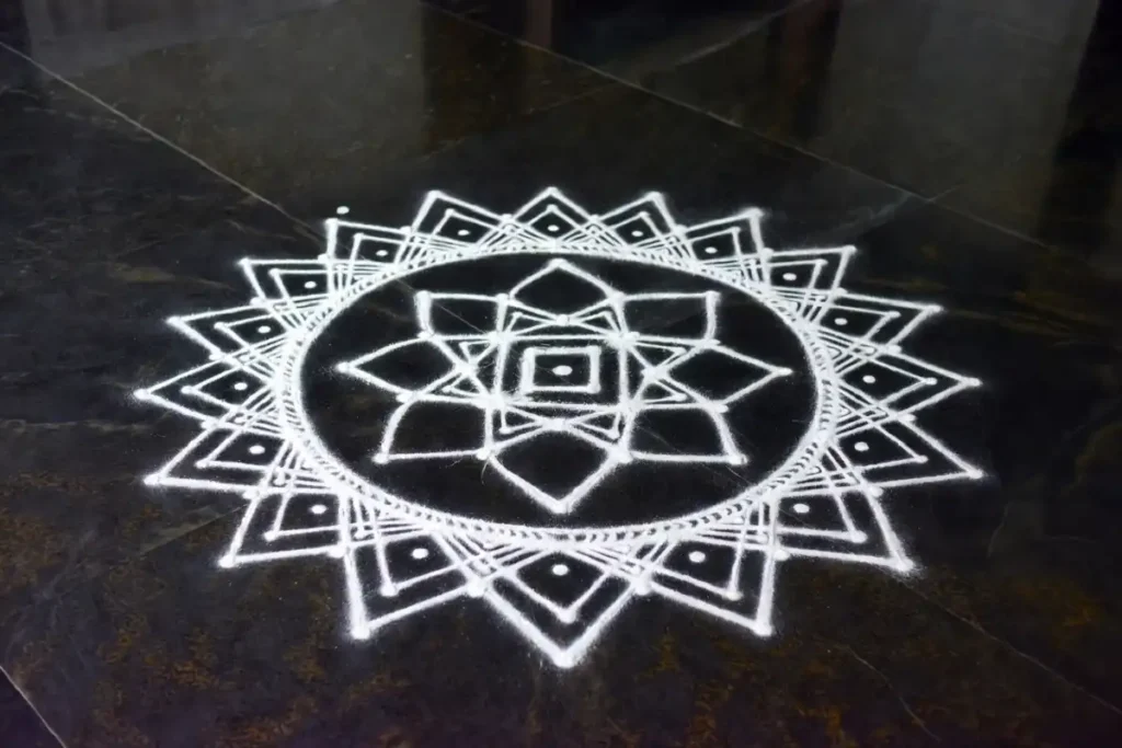 White rangoli design featuring lotus and geometric patterns on a dark floor
