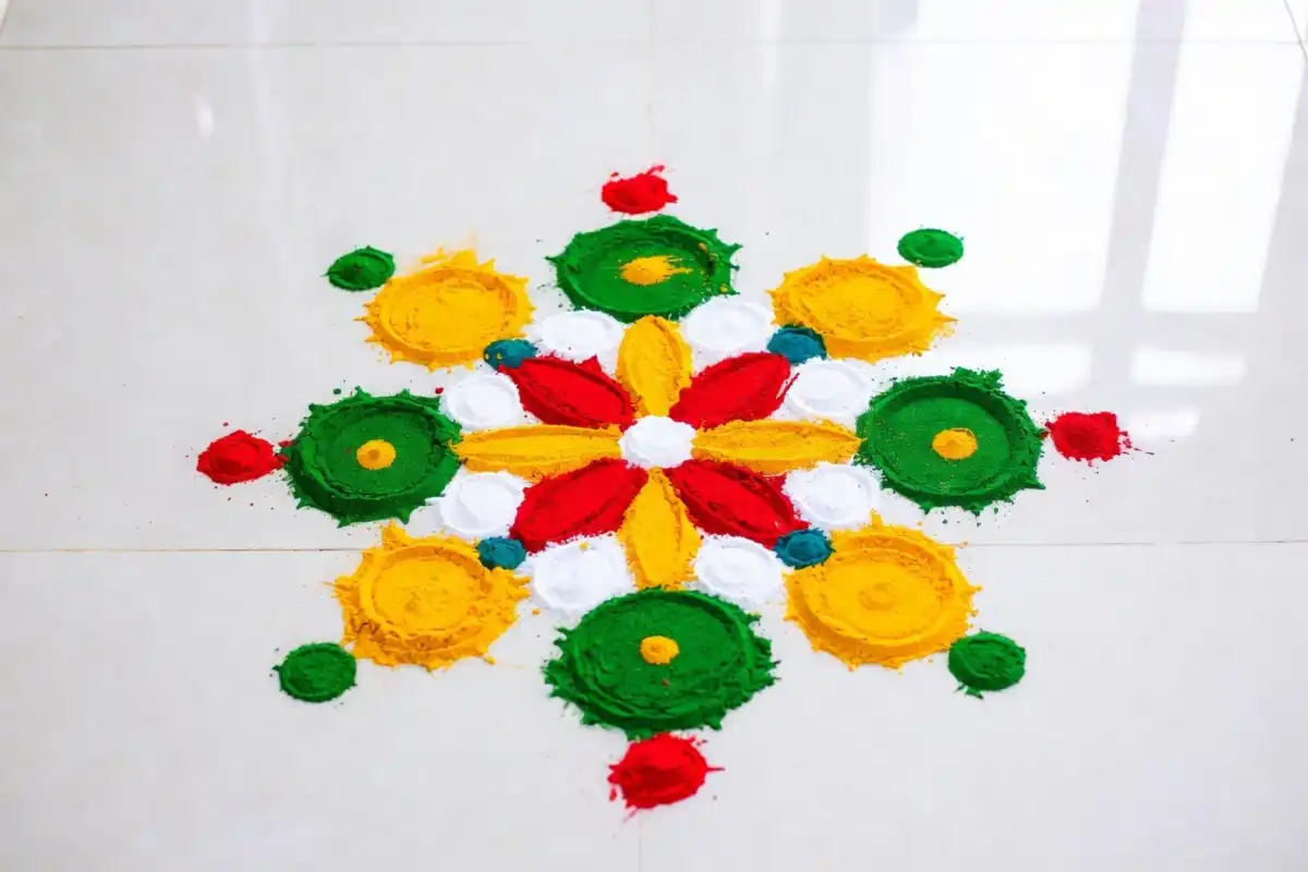 Colorful beginner friendly rangoli art design on white floor with flower and dot pattern
