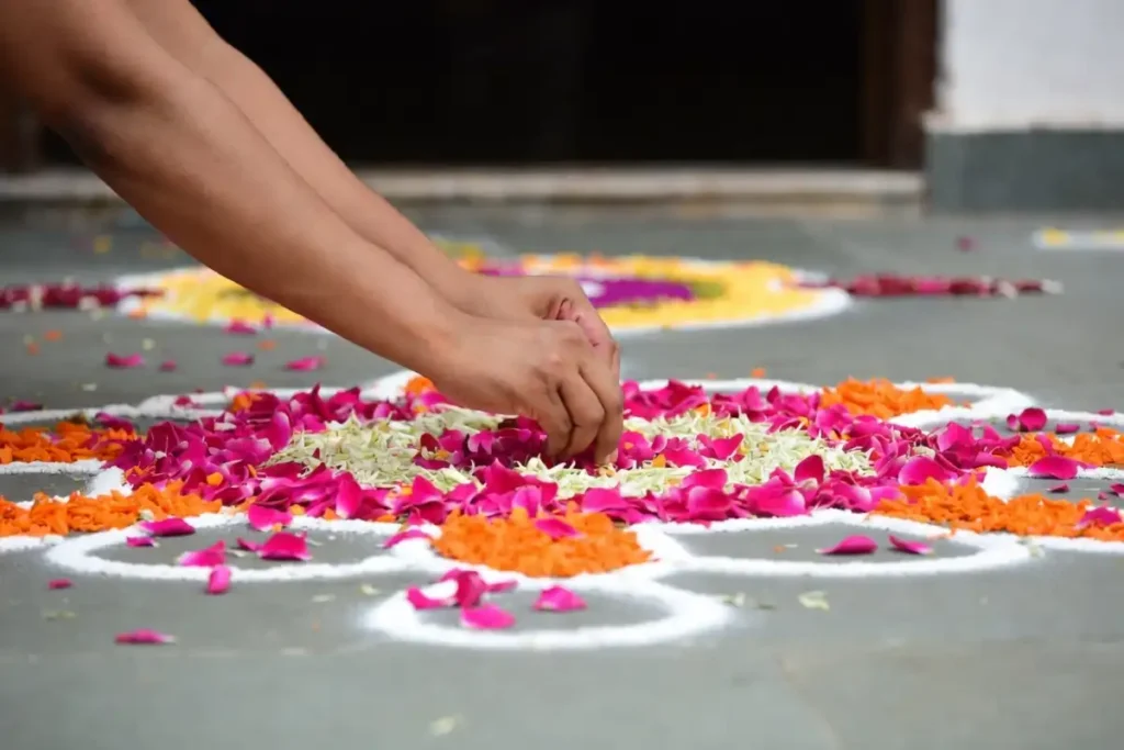 Hands creating a colorful entrance rangoli using bright flower petals on a stone floor