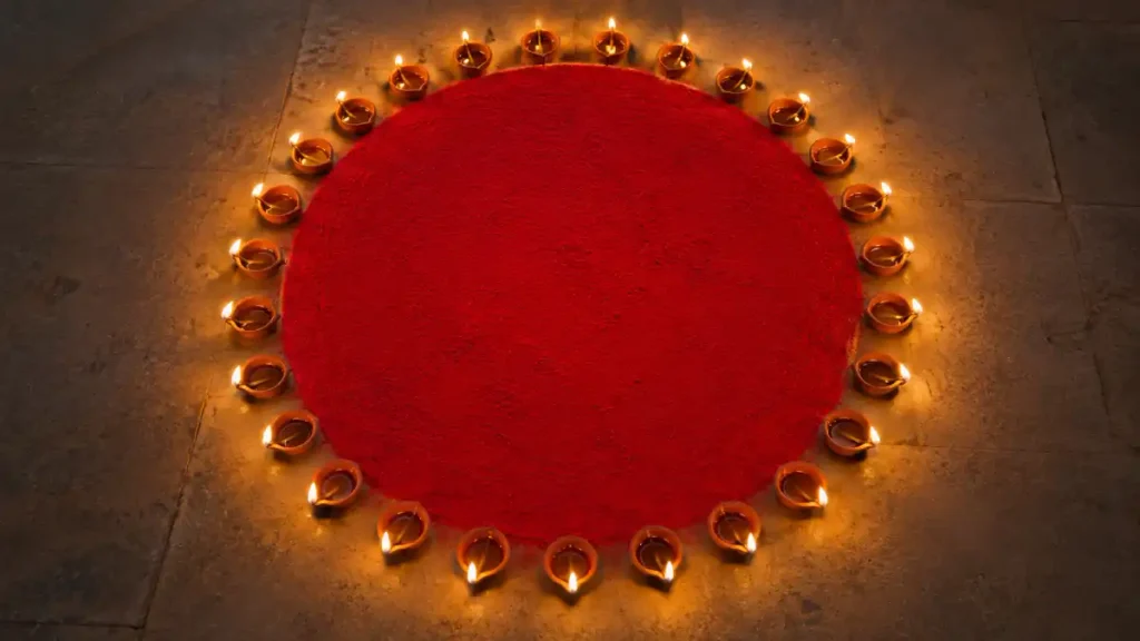 Red circular rangoli design bordered with small lit diyas for Diwali night