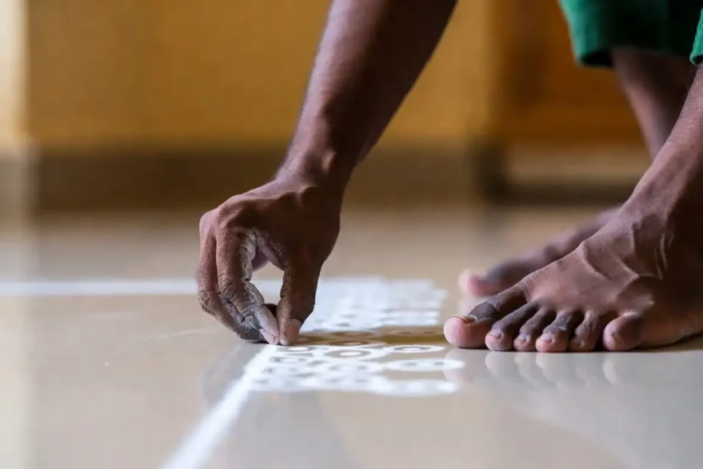 Beginner drawing a simple dot grid rangoli pattern on the floor with white powder