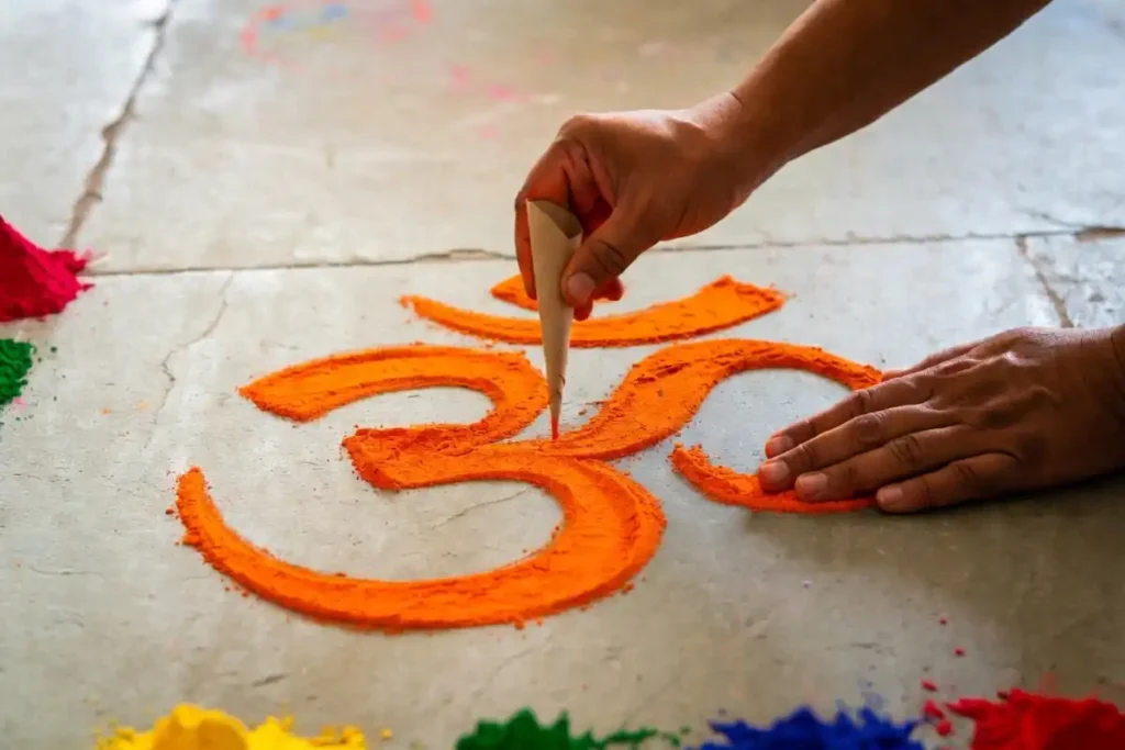 Hands applying rangoli powder through a paper cone to create an easy om rangoli design on a floor