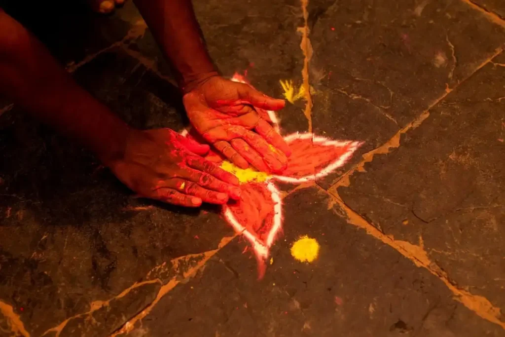 Hands drawing freehand petal rangoli without stencil easy on dark stone floor
