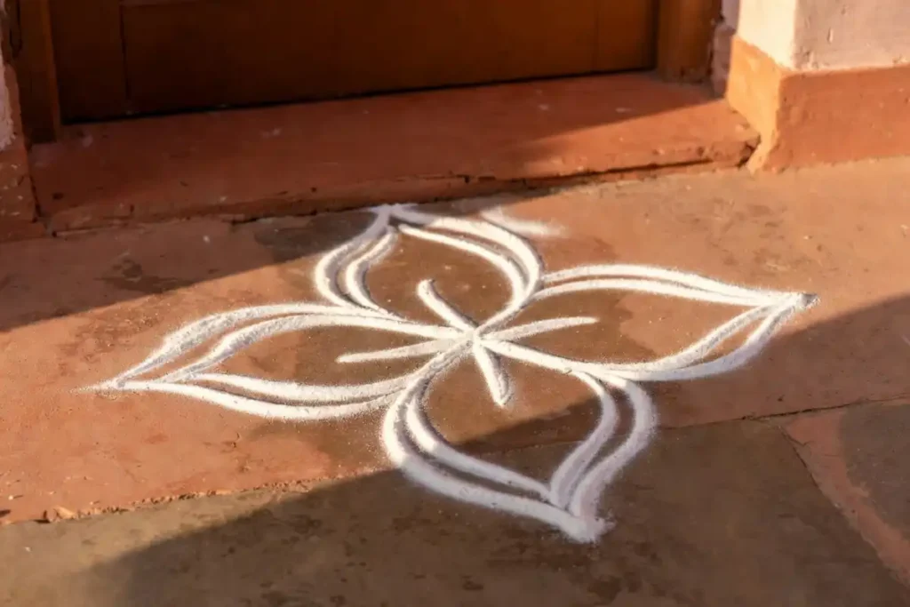 Simple minimal rangoli design with white rice flour on a traditional Indian doorstep