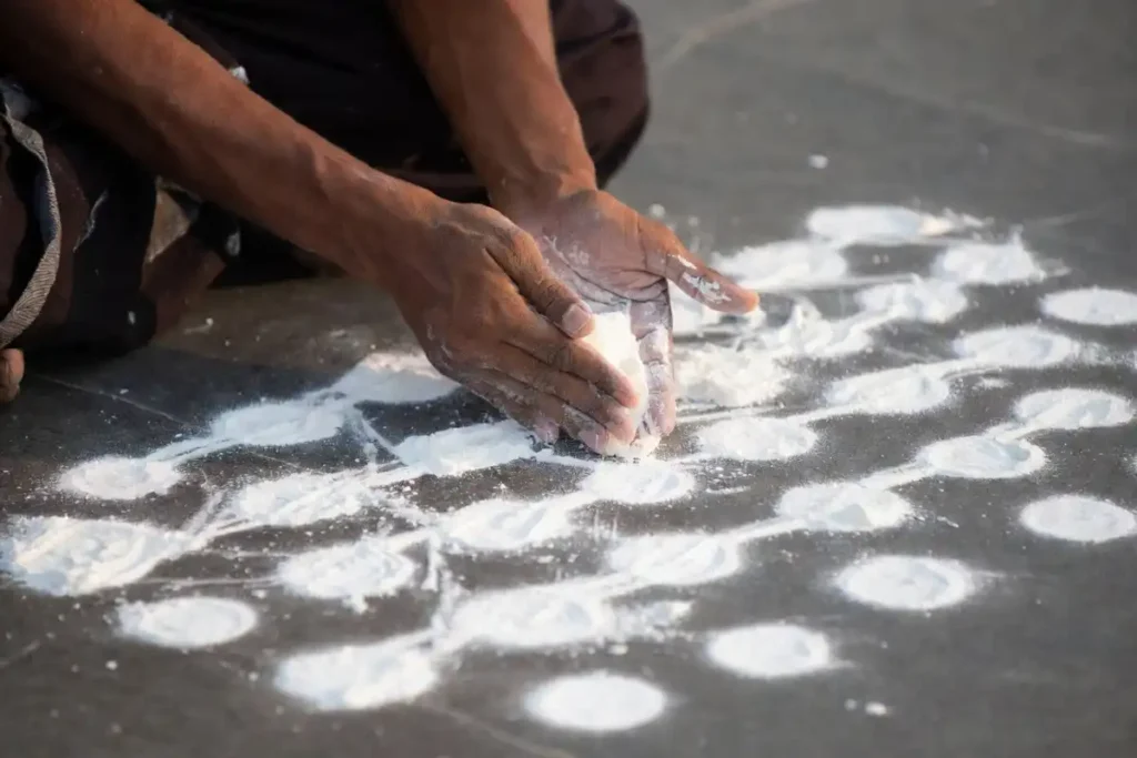 Hands creating a quick dot-based rangoli on a dark floor with chalk powder