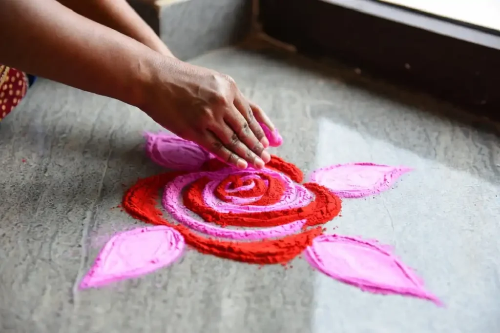 Hands filling a rose rangoli easy design with pink and red dry colors on stone floor