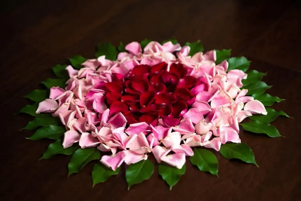 Completed rose rangoli easy design made with fresh pink and red petals on a dark wooden floor
