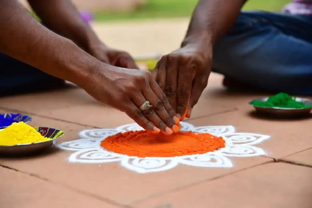 Hands filling a simple circle rangoli with orange powder using a circular template on a tiled floor