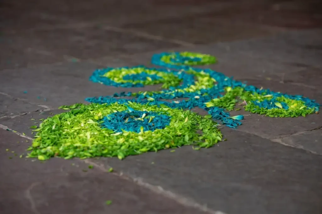 Small 3D rangoli peacock feather design with layered green and blue petals on dark floor