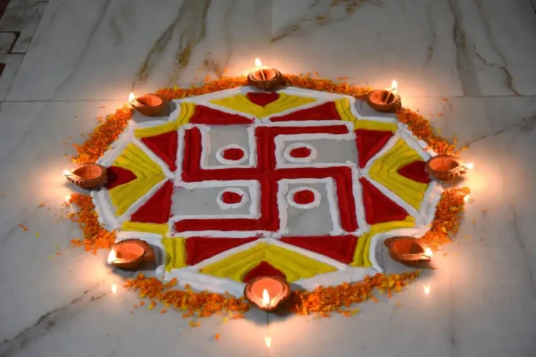 A colorful small swastik rangoli design on a marble floor surrounded by diyas and flower petals