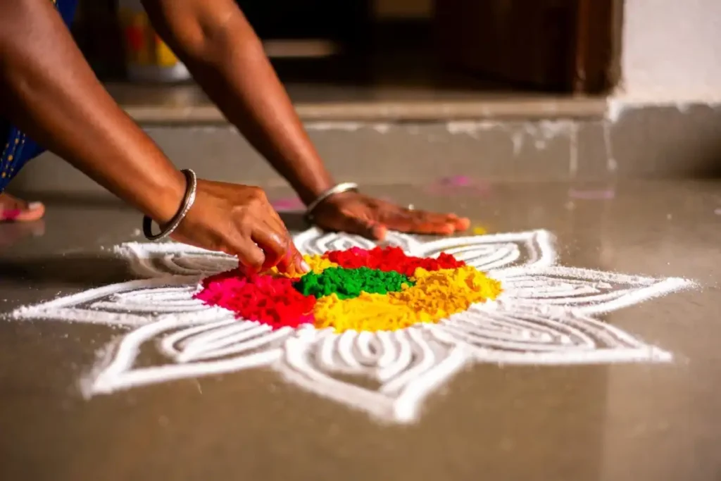 Person creating traditional rangoli designs for festivals using colored powder and rice flour